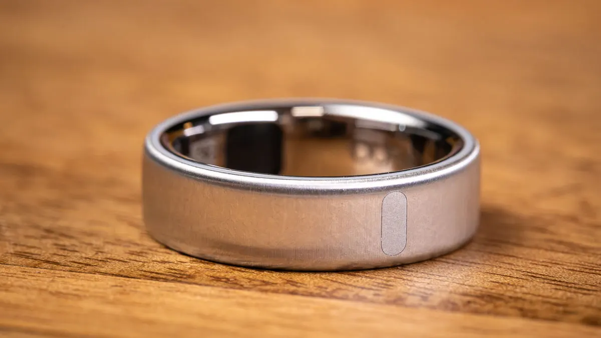 Der Oura Ring 5 in Brushed Silver liegt auf einem Holztisch. Zu sehen ist der Streifen, der die Position der Sensoren im Inneren verrät.