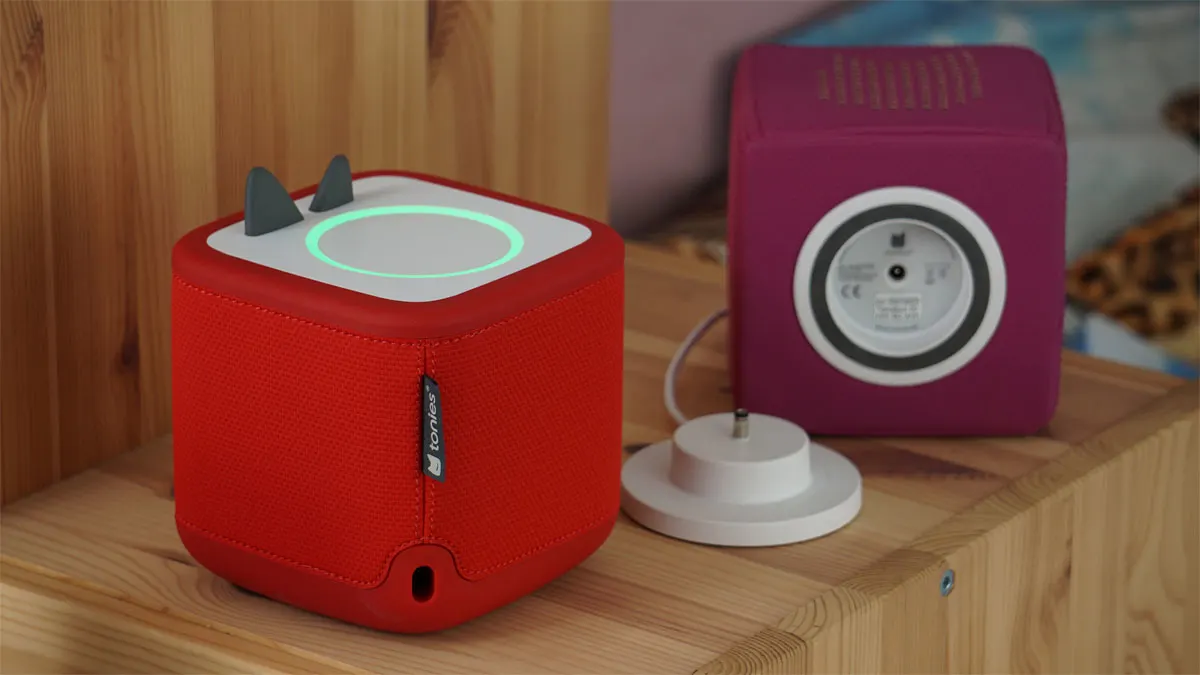 Auf der Rückseite der Toniebox 2 findet sich ein USB-C-Anschluss, an der Unterseite der Toniebox 1 ist der proprietäre Ladeanschluss zu sehen, daneben die weiße Ladestation.