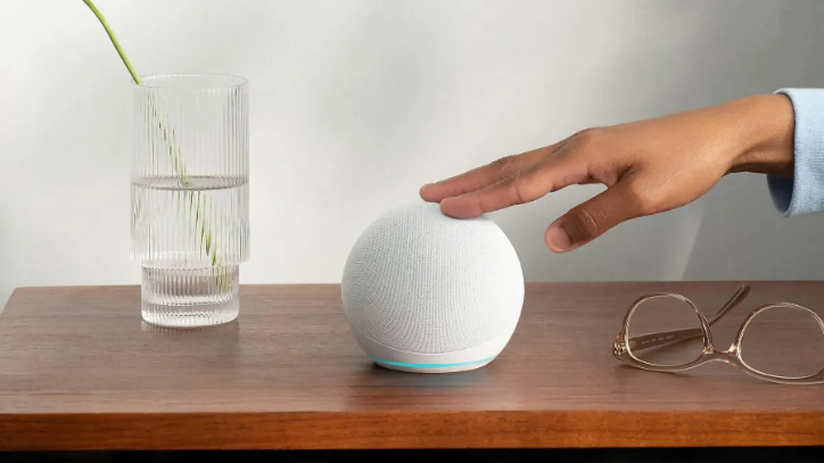 Ein Amazon Echo Dot auf einem Tisch neben einem Glas und einer Brille.
