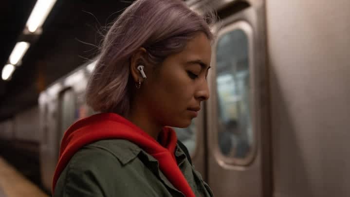 Eine Frau mit AirPods Pro im Ohr steht neben einer Bahn.
