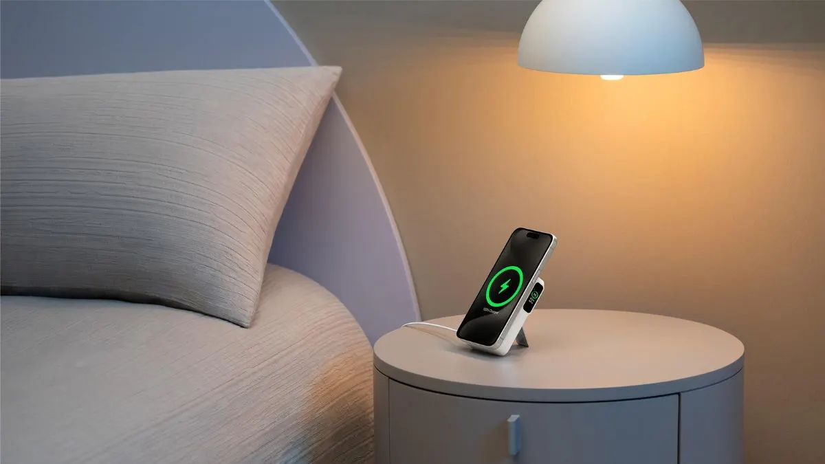 Die Powerbank Anker MagGo (A1654G21) steht mit ausgeklapptem Standfuß auf einem Nachttisch. An ihr haftet ein Smartphone, das gerade kabellos geladen wird.
