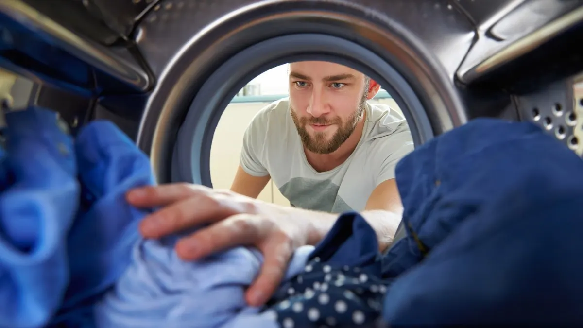 Ein Mann greift nach Wäsche im Inneren einer Waschmaschine.