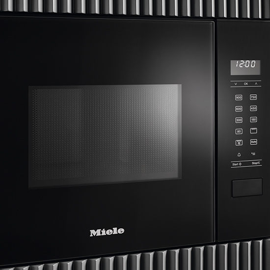 Eine schwarze Miele-Mikrowelle mit einem digitalen Bedienfeld, das 12:00 anzeigt, umgeben von einer geriffelten Oberfläche.