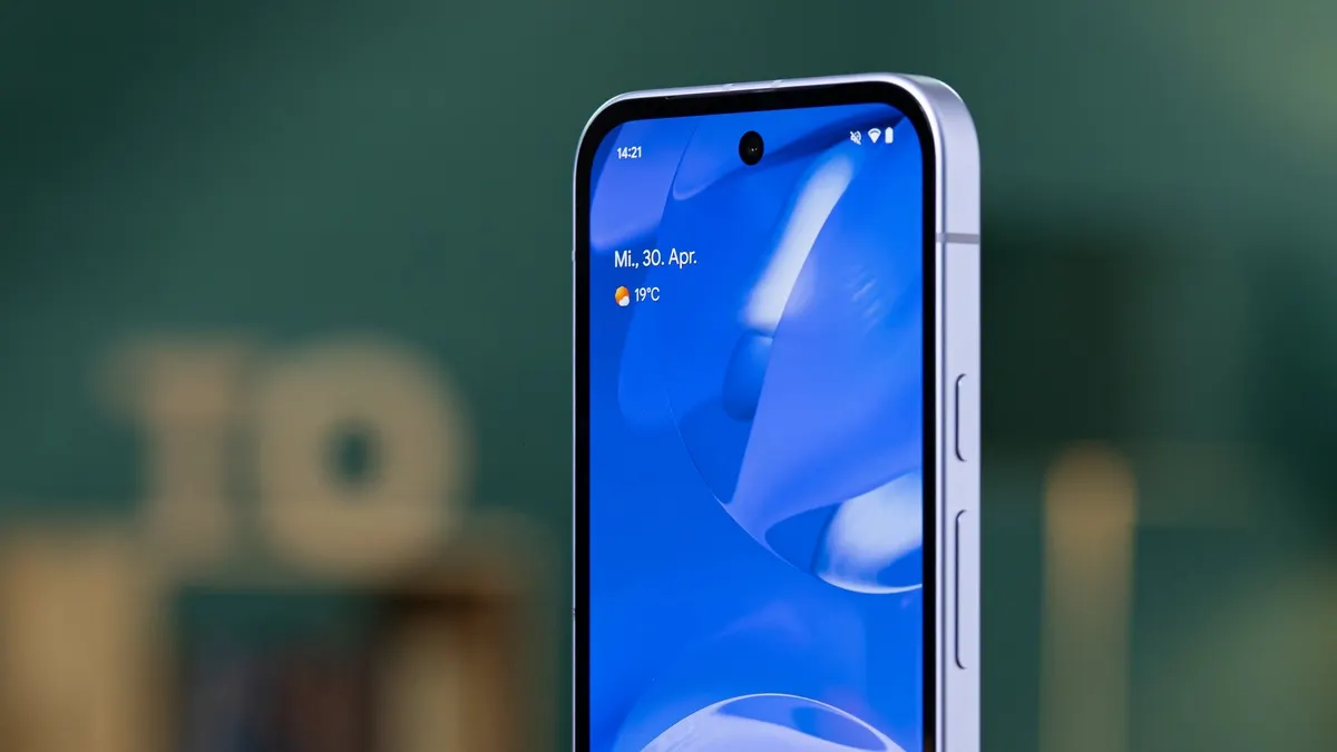 Ein silbernes Smartphone zeigt auf dem blauen Bildschirm die Uhrzeit 14:21, Mittwoch, 30. April und 19 Grad Celsius.