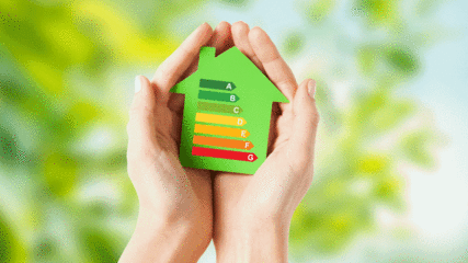 Frauenhände halten eine grüne Silhouette von einem Haus. Auf dem Haus zu sehen die Energieeffizienzklassen. 