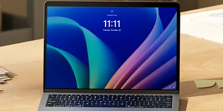 Ein Laptop steht auf einem Holztisch. Auf dem Bildschirm werden die Uhrzeit 11:11 und ein abstraktes, farbenfrohes Design angezeigt.