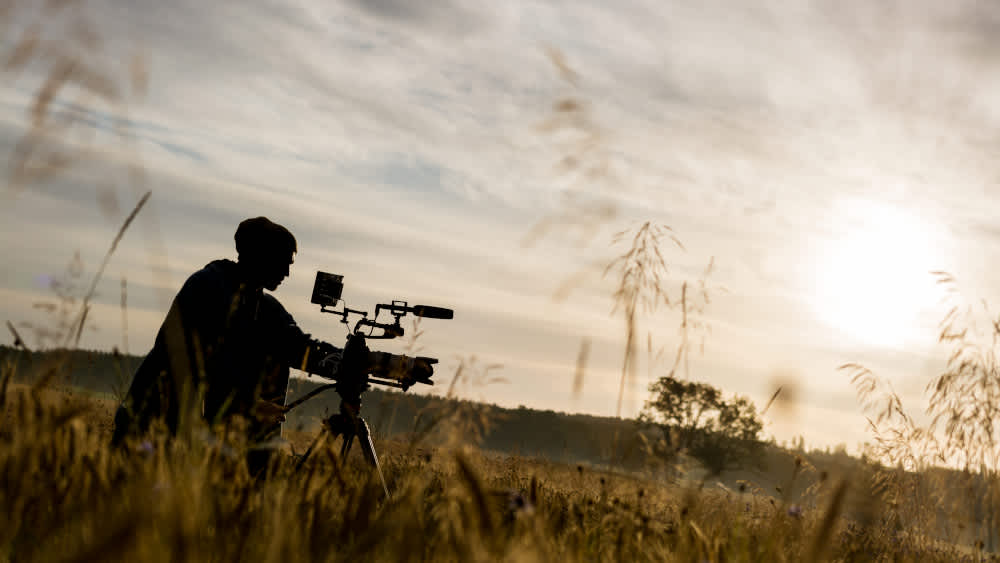 Ein Mann steht mit einer professionellen Kamera in einem Feld.