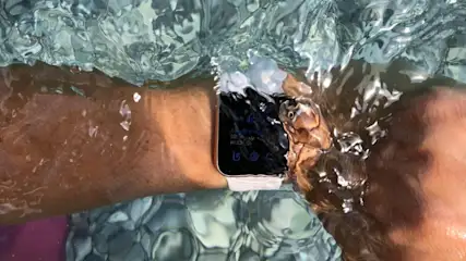 Ein Arm mit einer Smartwatch mit weißem Armband ist unter Wasser zu sehen. Das Wasser ist klar und bewegt sich.