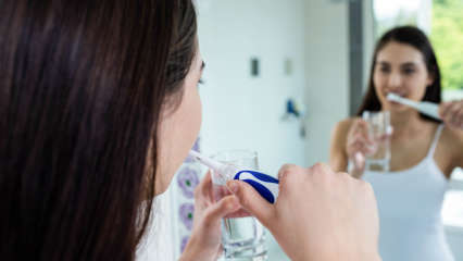 Eine Frau steht vor einem Spiegel und putzt mit einer elektrischen Zahnbürste ihre Zähne.