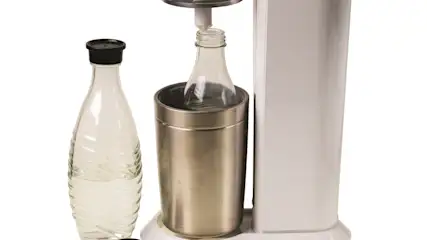 Eine weiße Soda-Maschine mit einer Flasche in einem Metallbehälter und einer separaten Flasche mit schwarzem Deckel.