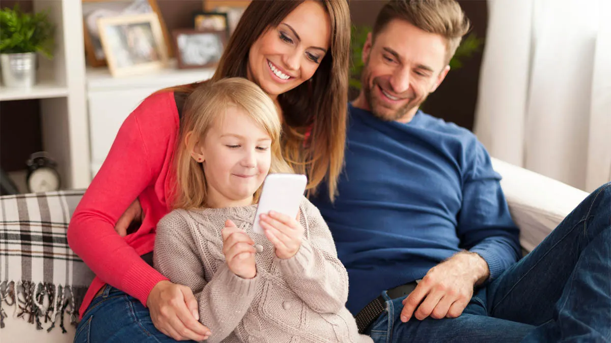 Eine Familie sitzt gemeinsam auf einer Couch und schaut auf ein Handy.