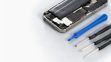 Geöffnetes Smartphone mit Batterie, blauer Öffner und drei schwarzen Schraubendrehern auf hellem Grund.