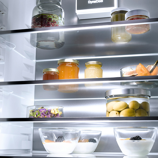 Ein Kühlschrank mit Glasregalen zeigt Gläser mit Marmelade, Obst und Joghurt mit Brombeeren.