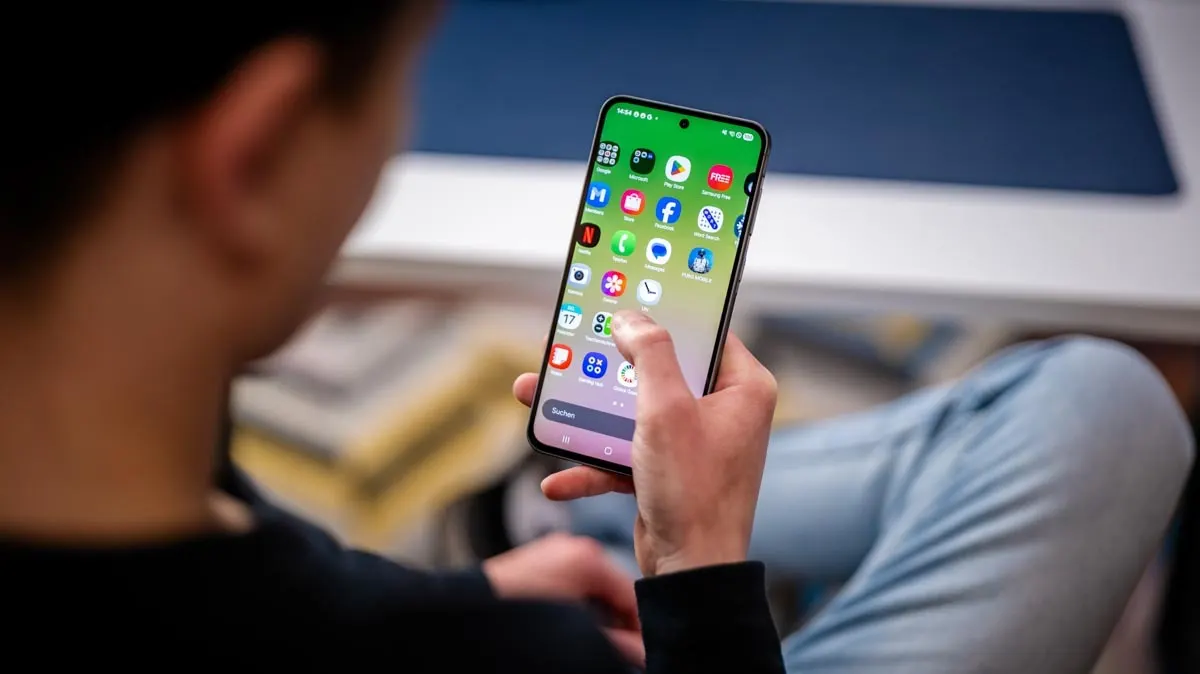 Eine Person sitzt an einem Tisch und hält das Smartphone Samsung Galaxy A56 in der Hand.