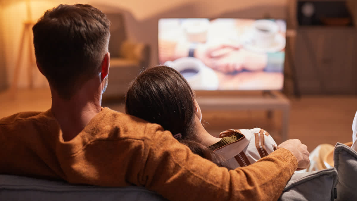Ein Paar schaut gemeinsam im Wohnzimmer einen Film im Fernsehen.