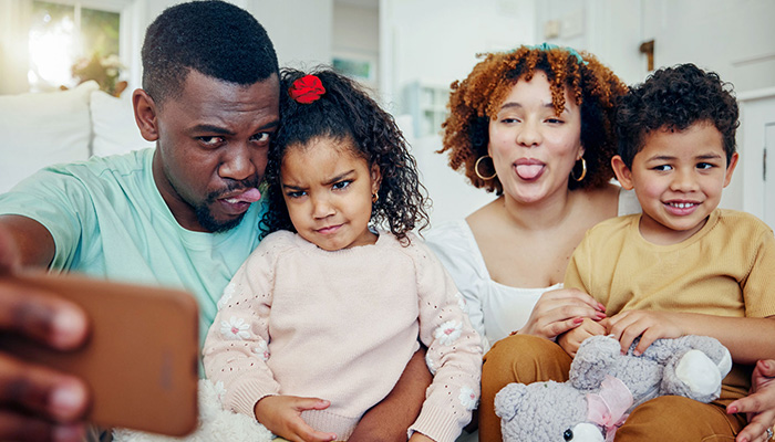 Eine Familie mit zwei Kindern macht ein Selfie, während sie Grimassen schneidet. Ein Teddybär ist im Bild.