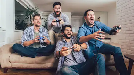 Gruppe von Männern sitzt aufgeregt auf einer Couch. Jeder hält einen Controller in der Hand.