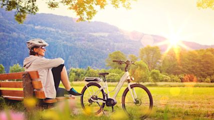 Eine Frau sitzt draußen auf einer Bank neben ihrem E-Bike.