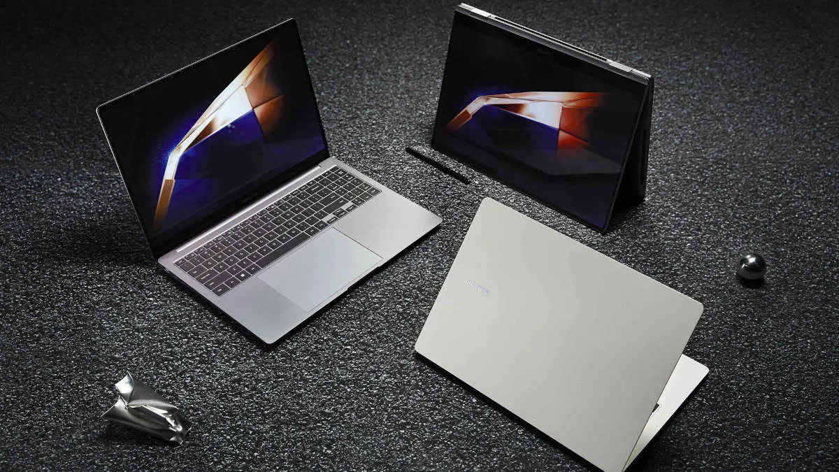 Auf einem dunklen, gesprenkelten Untergrund sind zwei Laptops, ein Stift und eine Metallkugel platziert. Ein Laptop ist geöffnet, einer geschlossen.