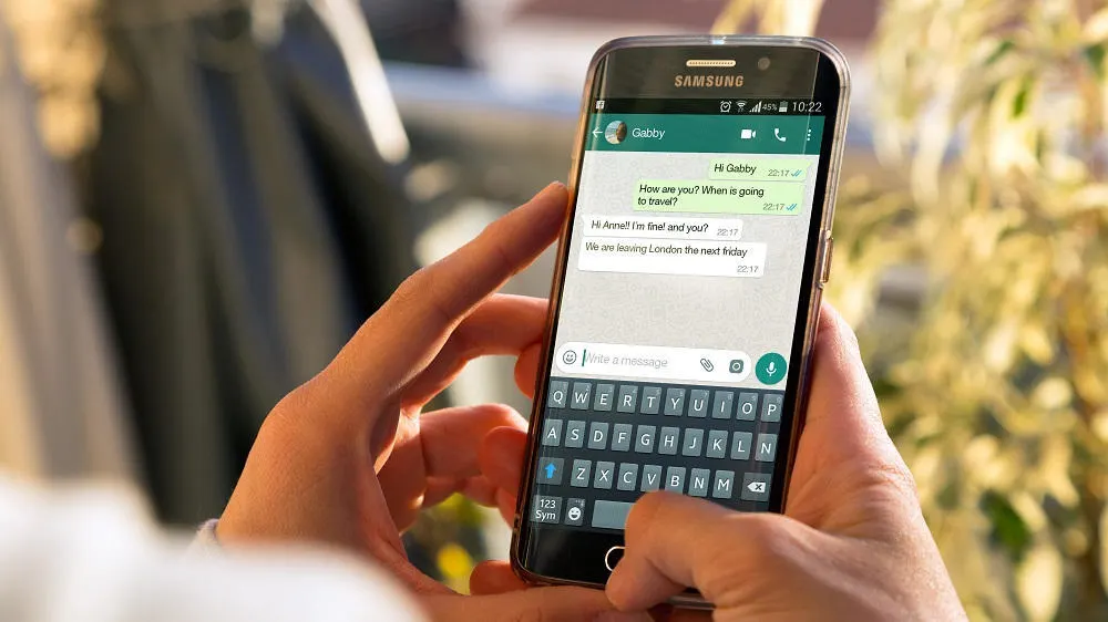 Eine Person hält ein Samsung-Smartphone, auf dem eine grüne Chat-App mit einer Tastatur geöffnet ist.