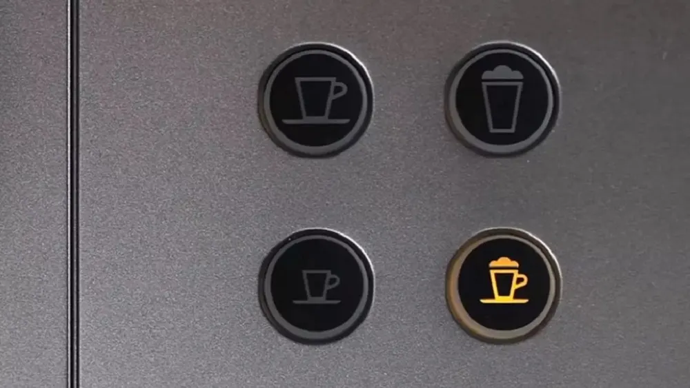 Vier schwarze Knöpfe auf einer grauen Oberfläche. Die Knöpfe zeigen Symbole für Tasse, Becher und Kaffeetasse. Ein Knopf leuchtet gelb.