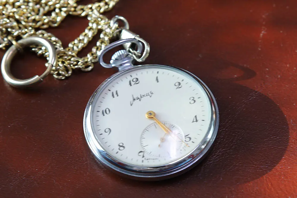 Eine Taschenuhr mit goldenen Zeigern und einer goldenen Kette liegt auf einer braunen Oberfläche.
