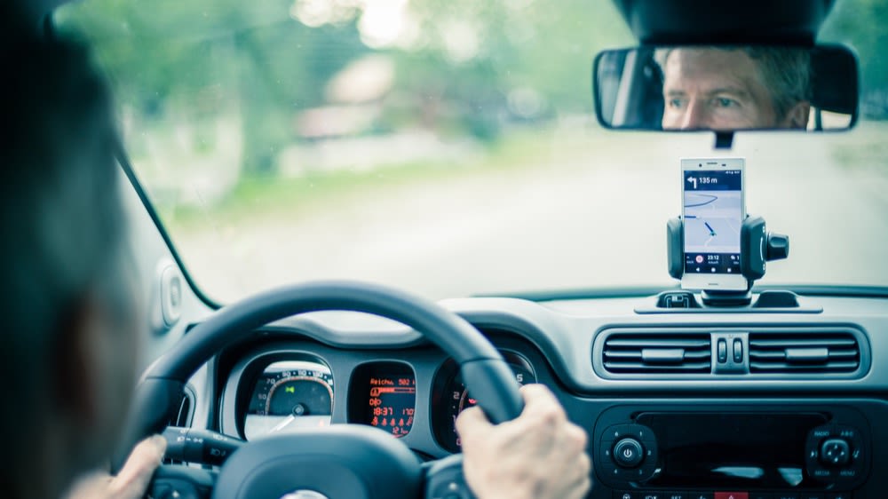 Ein Mann fährt im Auto und nutzt ein Smartphone als Navigationsgerät.