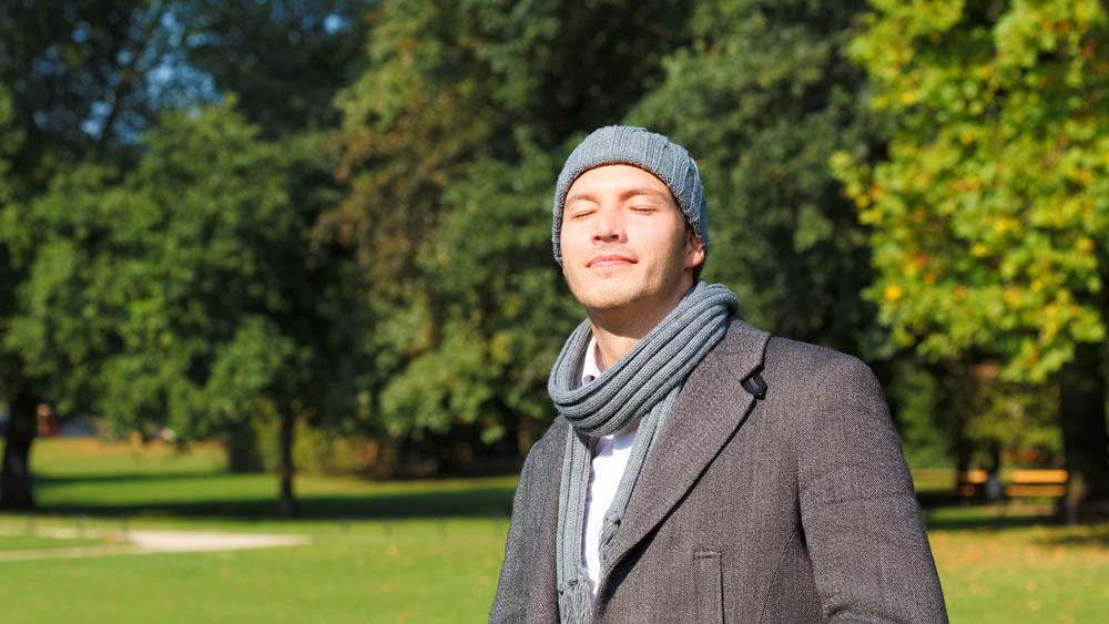 Ein Mann steht draussen im Park und hält sein Gesicht in die Sonne.