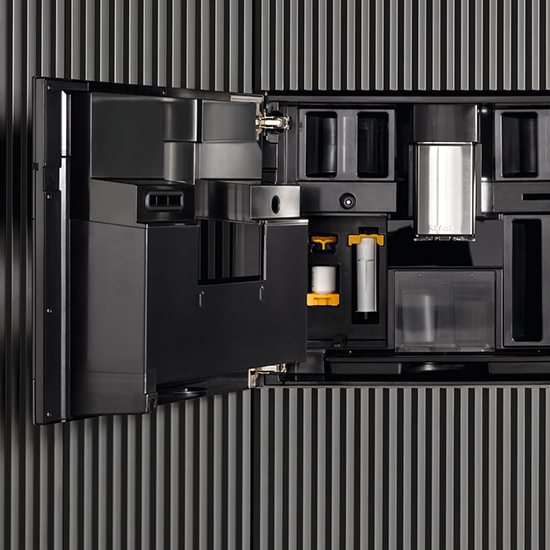 Schwarzer Kaffeevollautomat mit geöffneter Tür, eingebaut in eine Wand mit vertikalen Streifen. Silberner Behälter sichtbar.