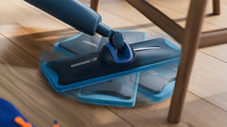 Ein Philips OneUp steht auf einem Holzboden, teilweise unter einem Holzstuhl. Man sieht wie sich der Mopp um 360 Grad drehen kann.