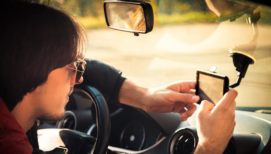 Ein Mann mit Sonnenbrille justiert ein Gerät mit Saugnapfhalterung im Auto. Rückspiegel sichtbar.