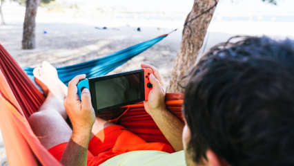 Ein Mann benutzt eine Nintendo Switch in einer Hängematte.