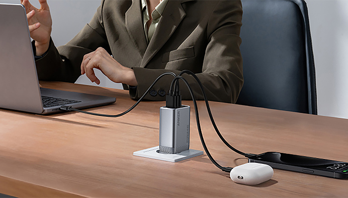 Geschäftsperson am Schreibtisch mit Laptop, silberner USB-Hub mit Kabeln und Computer-Maus auf hellem Holztisch im Büro.