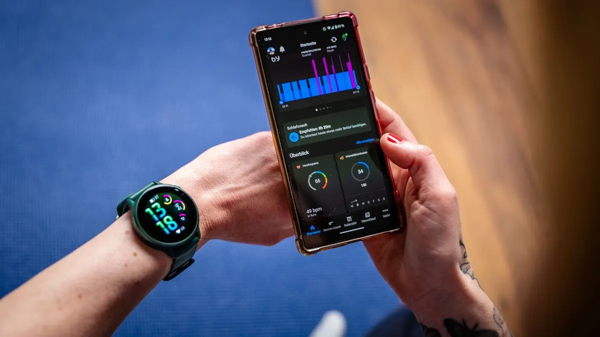 Eine Person hält ein Smartphone mit einer Fitness-App in der Hand und trägt eine grüne Smartwatch am Handgelenk.