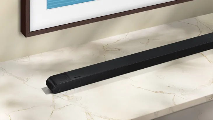 Ein schwarzer Lautsprecher liegt auf einem marmorierten Tisch unter einem gerahmten Bild an der Wand.