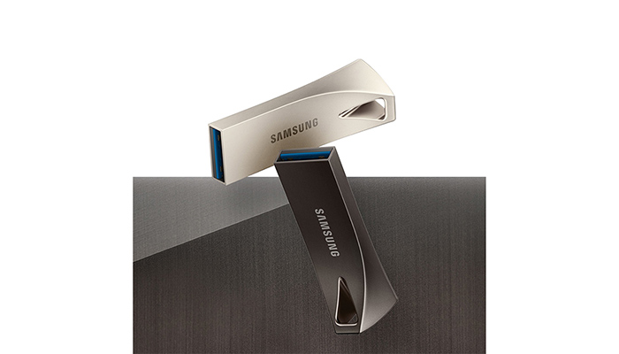 Zwei Samsung USB-Sticks liegen auf einer grauen Oberfläche. Einer ist silberfarben, der andere dunkelgrau mit blauen Akzenten.