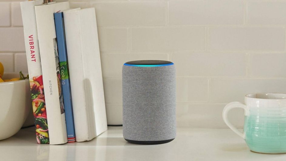 Amazon Echo Dot steht auf einem Regal und blinkt blau. Daneben stehen Bücher und eine Tasse.