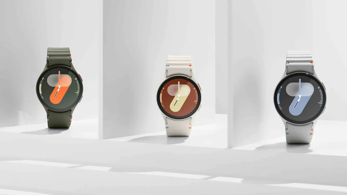 Drei Smartwatches mit Armbändern in Grün, Weiß und Grau zeigen ein digitales Zifferblatt mit stilisierter Sieben vor weißem Hintergrund.