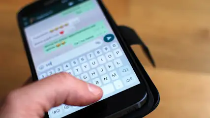Nahaufnahme eines Smartphones, das in einer Hand gehalten wird und einen Chatbildschirm mit Tastatur anzeigt.