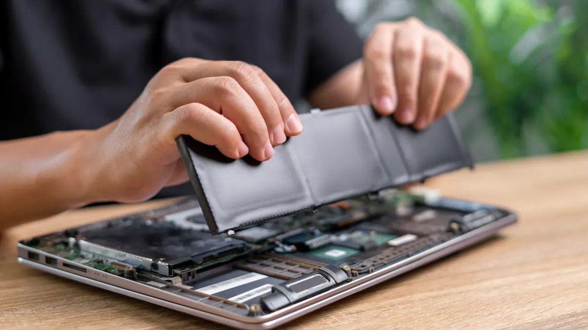 Eine Person entfernt den Akku aus dem Gehäuse eines Laptops.