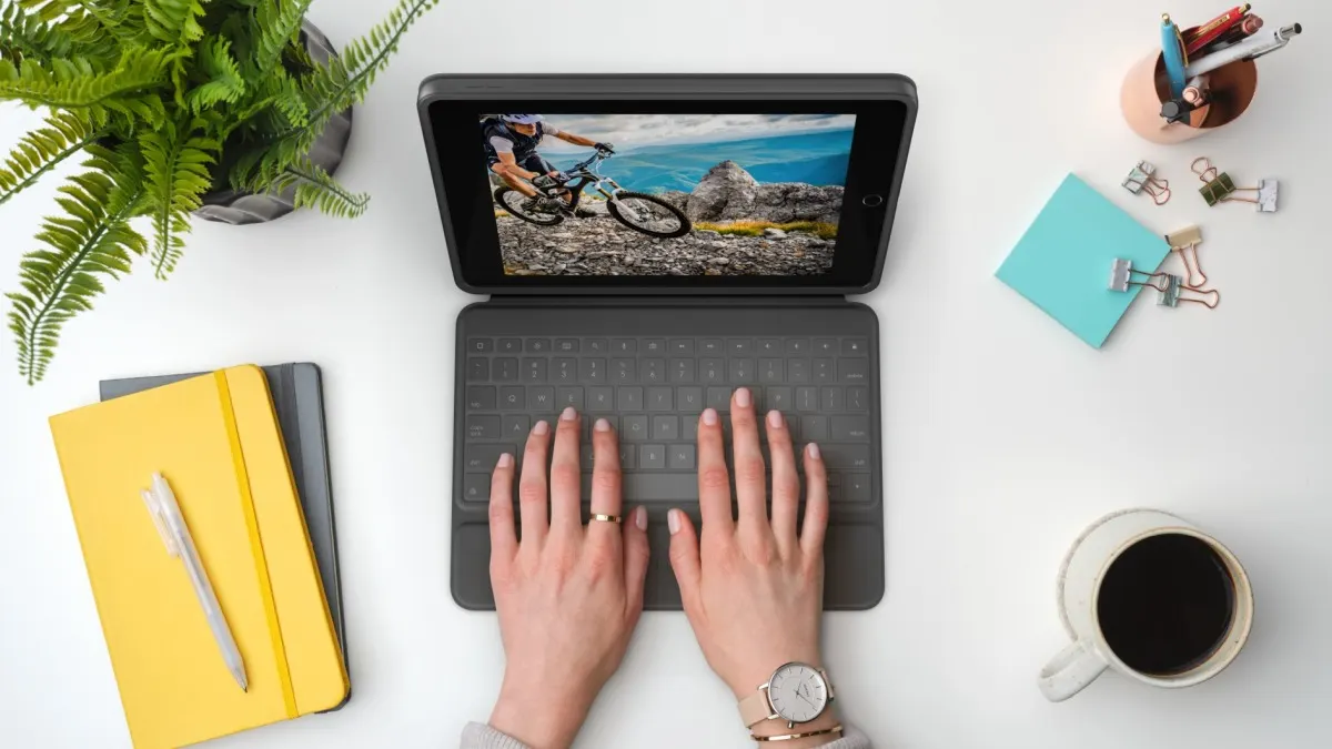 Eine Person tippt an einem Tisch auf der Tastatur der iPad-Hülle Logitech Rugged Folio.