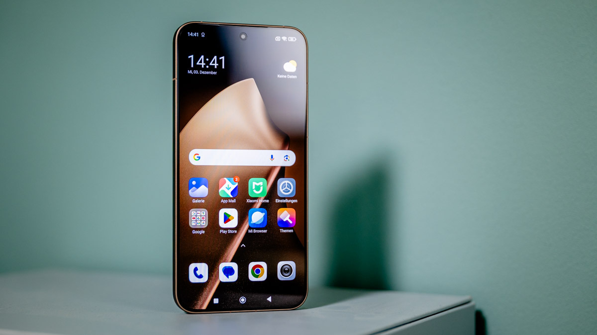Das Smartphone Xiaomi 15T Pro steht mit eingeschaltetem Display vor einer grünen Wand.