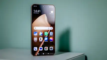 Das Smartphone Xiaomi 15T Pro steht mit eingeschaltetem Display vor einer grünen Wand.