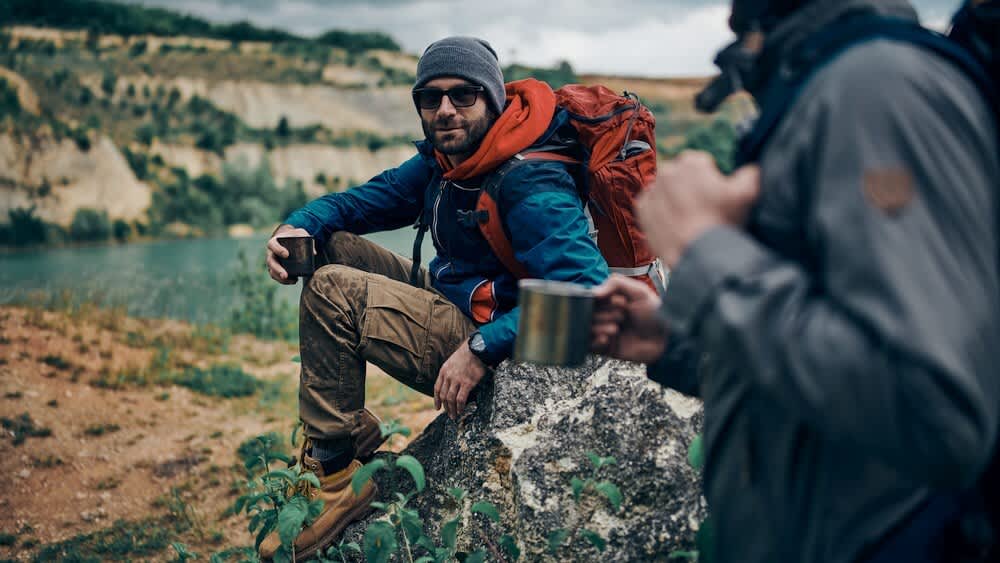 Zwei Männer trinken Tee beim Wandern in der Natur.