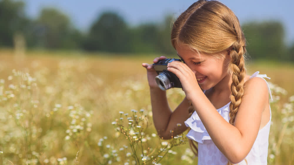 Ein kleines Mädchen fotografiert mit einer Kamera eine Wiese.