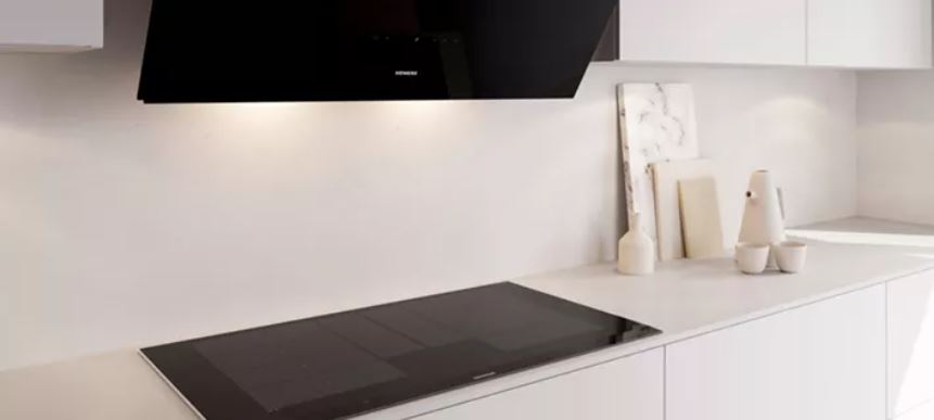 Minimalistische Küche mit schwarzem Kochfeld unter Dunstabzugshaube, weißer Arbeitsfläche und Deko-Elementen.
