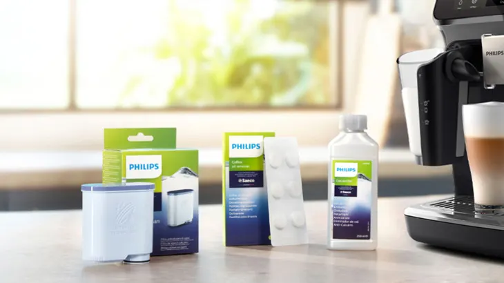 Eine Sammlung von Philips-Kaffeemaschinenzubehör, einschließlich Filter, Entkalker und Reinigungstabletten, vor einem Fenster.
