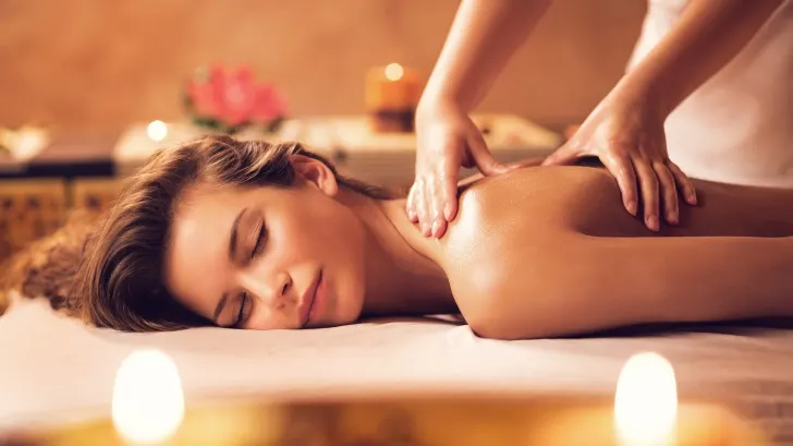 Eine Frau liegt auf einer Liege und bekommt eine Rückenmassage. Kerzen und Blumen dekorieren den Raum.