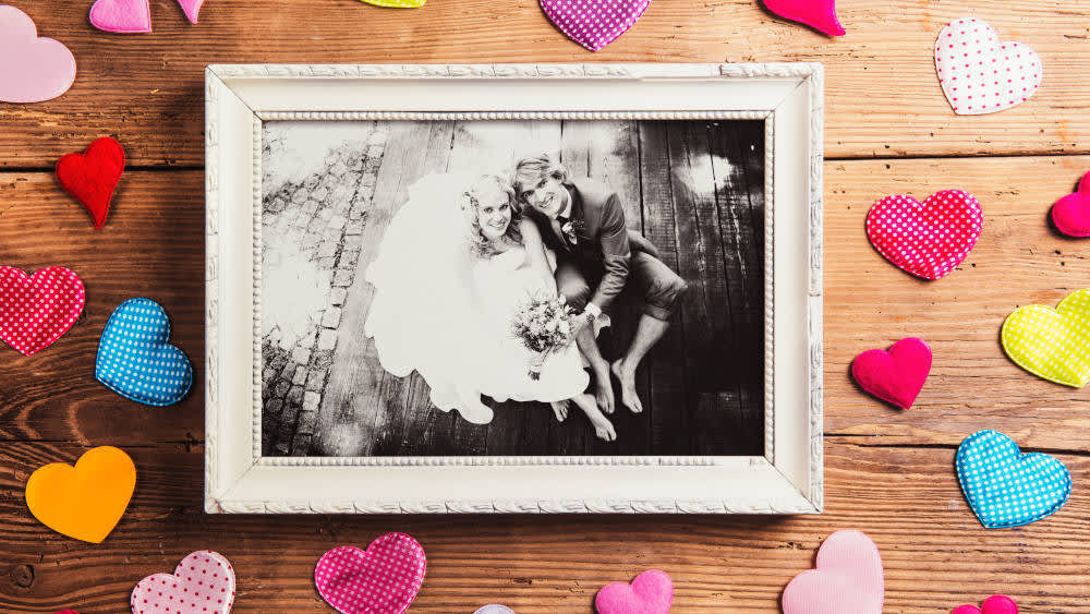 Ein eingerahmtes Schwarz-Weiß-Foto eines Hochzeitspaares liegt auf einem Holztisch mit Dekoherzen.