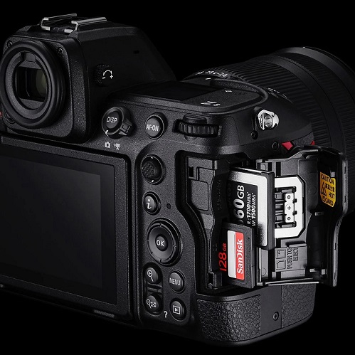 Nahaufnahme einer schwarzen Kamera mit zwei Speicherkarten. Eine SanDisk-Karte mit 128 GB ist sichtbar. Mehrere Tasten sind auf der Seite der Kamera angeordnet.